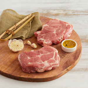 Dos Bifes de Bondiola de Cerdo Crudos marca Sagal sobre tabla de cortar y adornados con ajo y aceite