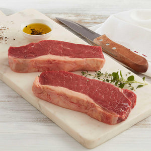 Dos Bifes de Chorizo, o también conocido  como New York Steak crudos marca Sagal sobre tabla de cortar adornados con cuchillo, aceite de oliva y tomillo