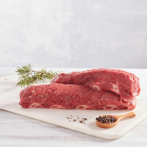 dos asados de tira de res crudos sobre una tabla de cortar con pimienta y romero