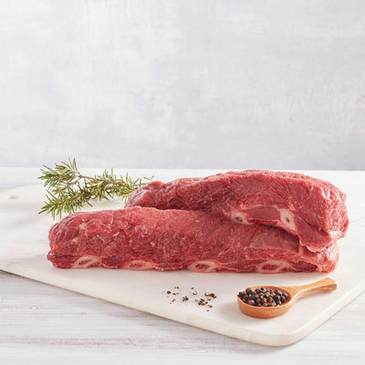 dos asados de tira de res crudos sobre una tabla de cortar con pimienta y romero