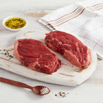 Dos bifes de Asado de Vacío marca Sagal crudos sobre tabla de cortar adornados con aceite y sal gruesa