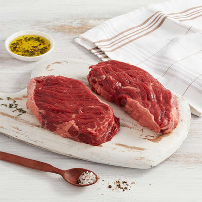 Dos bifes de Asado de Vacío marca Sagal crudos sobre tabla de cortar adornados con aceite y sal gruesa