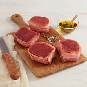 Cuatro Medallones de Lomo Res Crudos Envueltos en Tocineta Marca Sagal sobre Tabla de Cortar y Adornados con Aceite y Especias