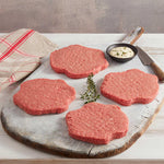 Cuatro Hamburguesas Premium de Res marca Sagal sobre tabla de cortar adornada de salsas, cuchillos para cortar y servilleta