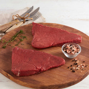 Dos tajadas de Sirloin de Res Marca Sagal Servidas sobre una tabla y acompañadas de sal gruesa y pimienta entera